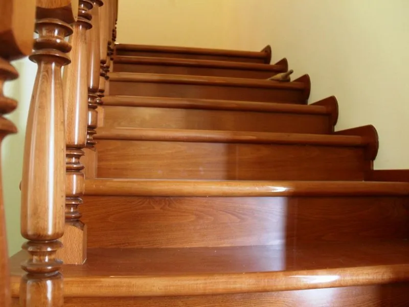 Polished wooden staircase with turned balusters and a plain light-colored wall in the background.