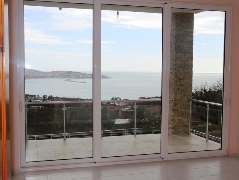 Panoramic windows in the living room of a house in Shushan, Montenegro, with access to the terrace and views of the sea and mountains.