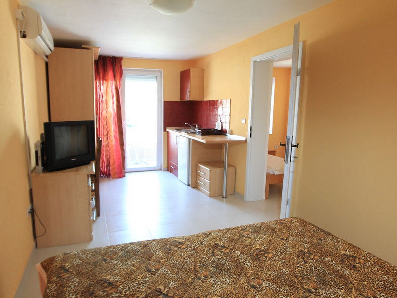 Living room with kitchen interior in a hotel in Budva, Montenegro: light furniture, bed with a leopard-print bedspread, access to the balcony.
