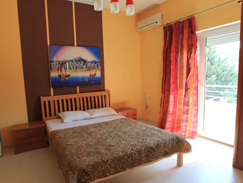 Bedroom featuring a wooden bed, nightstands, red curtains, and a cityscape painting.