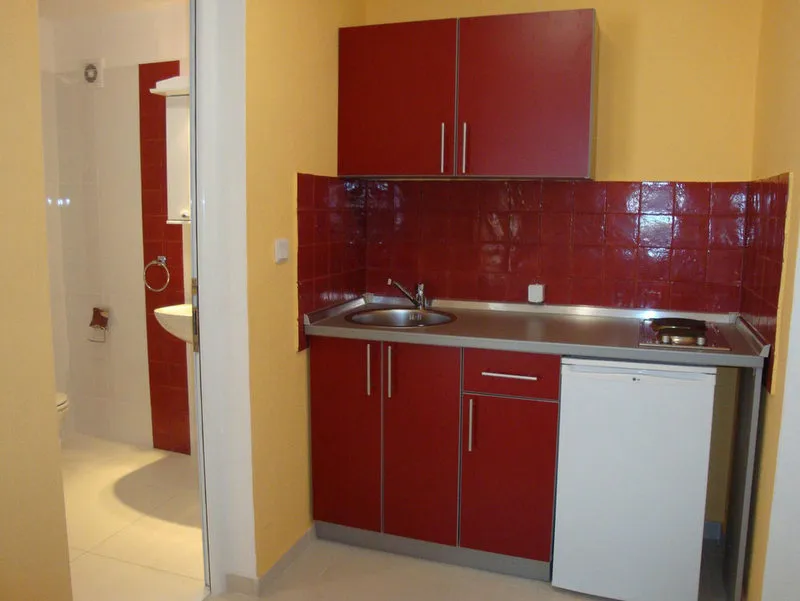 Kitchen with red cabinets, metal countertop, sink, and stove against a yellow wall.