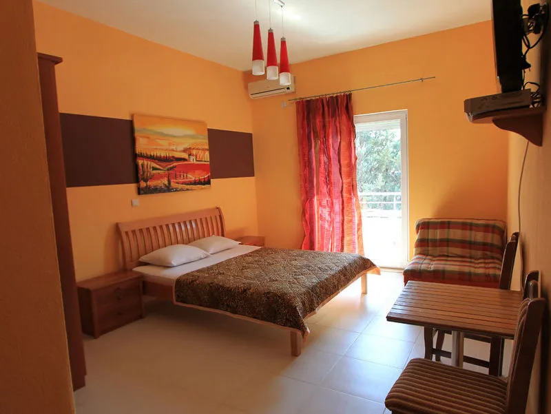 Bedroom with wooden bed, orange walls, small dining table, plaid sofa, and red curtains.