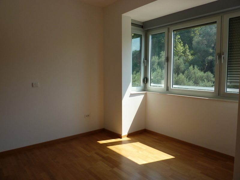 Bright bedroom with parquet flooring and a view of greenery in an apartment in Pržno, Montenegro. Empty room with large windows.