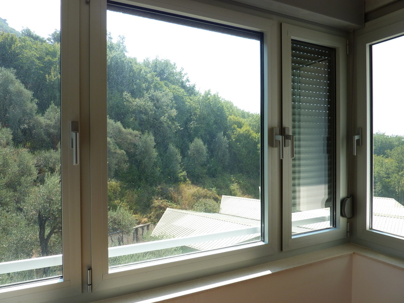 View from the living room window onto a green forest landscape in an apartment in Pržno, Montenegro, modern double-glazed windows with blinds.
