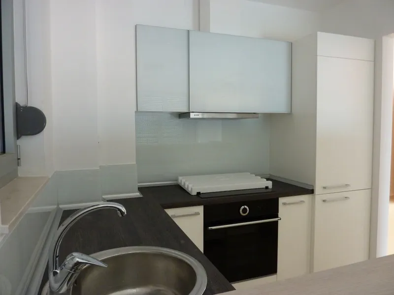 Modern kitchen with white glossy cabinets, dark countertop, built-in oven, sink, and range hood.