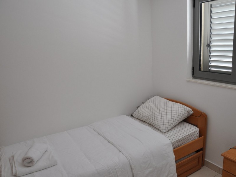 Bright bedroom with a single bed in an apartment in Bečići, Montenegro, with a window and blinds in a modern interior.