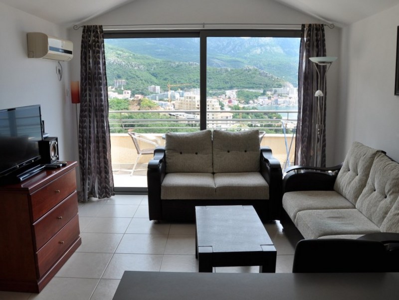 Living room with panoramic sea and mountain views in an apartment in Bečići, Montenegro: soft seating, terrace, and TV area.