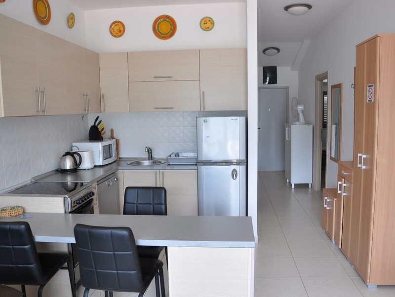 Bright kitchen-living room with light-toned furniture in an apartment in Bečići, Montenegro: breakfast bar and appliances.