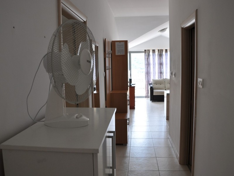 Bright hallway in an apartment in Bečići, Montenegro: white furniture, tiled floor, and a view of the living room with a panoramic window.