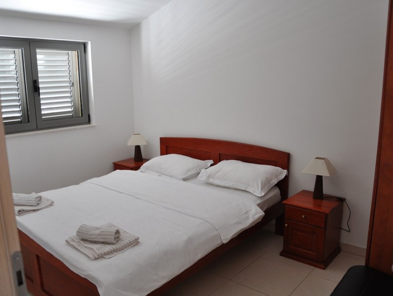 Bedroom with a double bed and bedside tables in an apartment in Becici, Montenegro. Light finishes and a window.