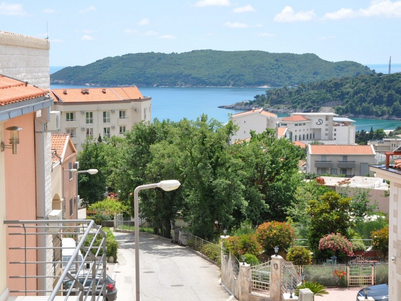 View from the apartment balcony in Bečići, Montenegro: a panorama of the sea, St. Nicholas Island, and a green resort area.