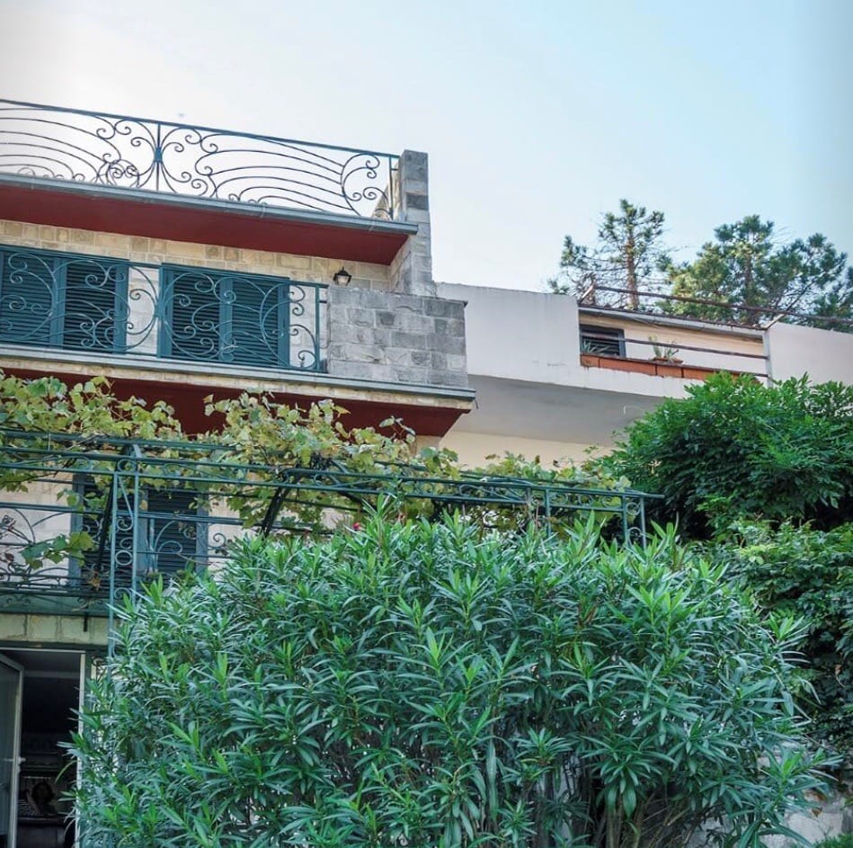 Villa facade in Stoliv, Montenegro: stone cladding, wrought-iron balconies, and a terrace with a vineyard in a green garden.