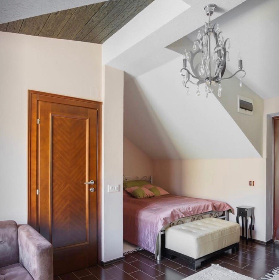 Bedroom in the villa attic in Stoliv, Montenegro: double bed, crystal chandelier, and wooden door.