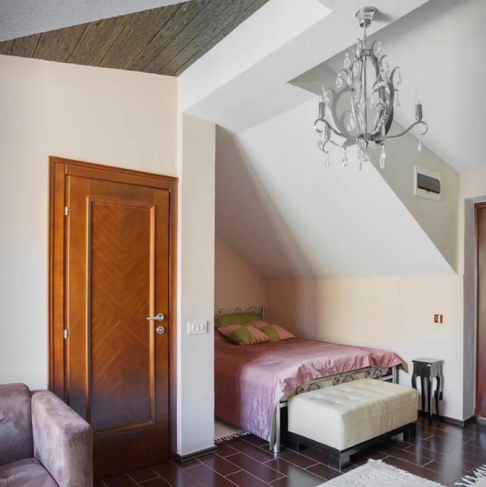 Bedroom with a single bed under a sloped ceiling, crystal chandelier, and wooden door visible.