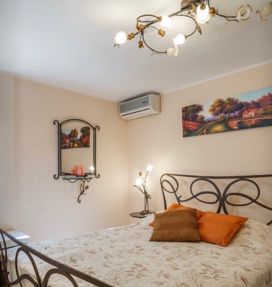Bedroom with a wrought-iron bed and designer lighting in a villa in Stoliv, Montenegro. Cozy interior with paintings.