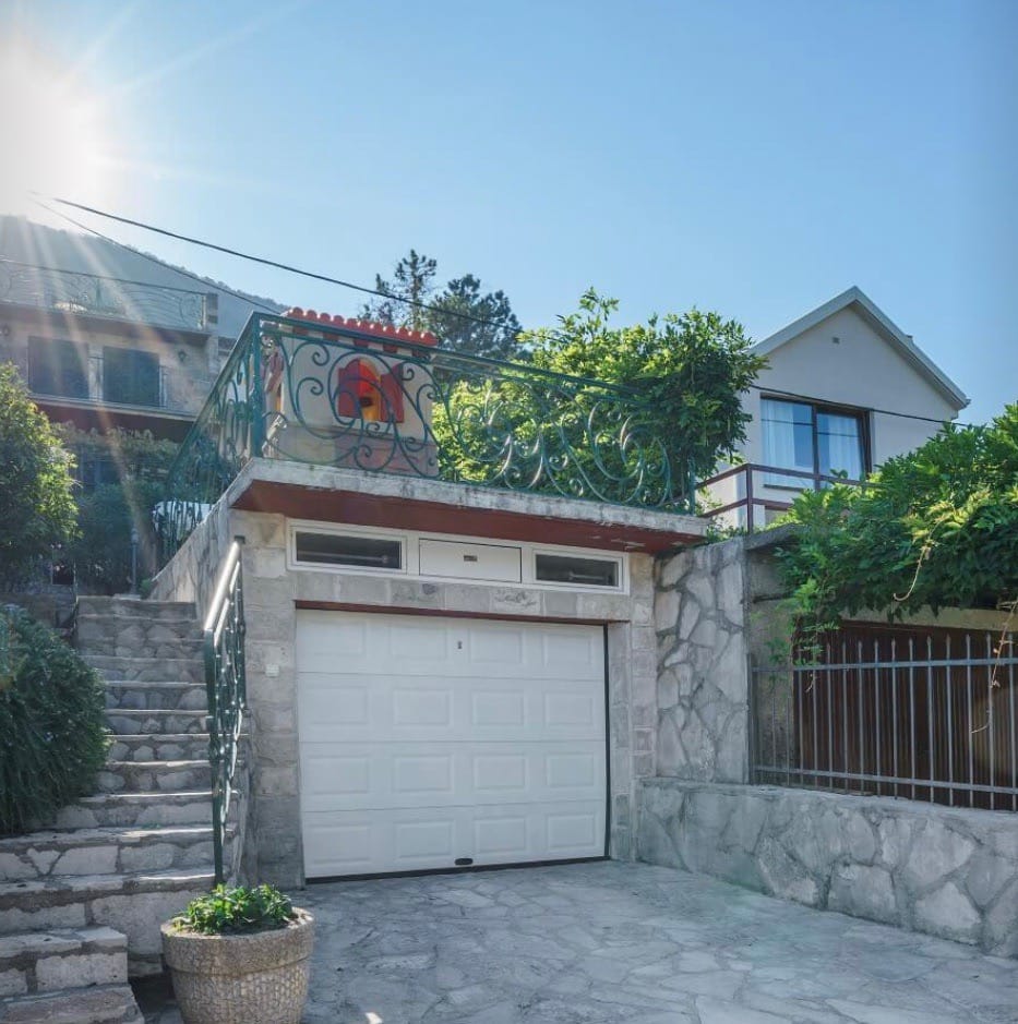 Private house with a garage, stone cladding, and a terrace in Stoliv, Montenegro. View of the villa with stairs and a garden.