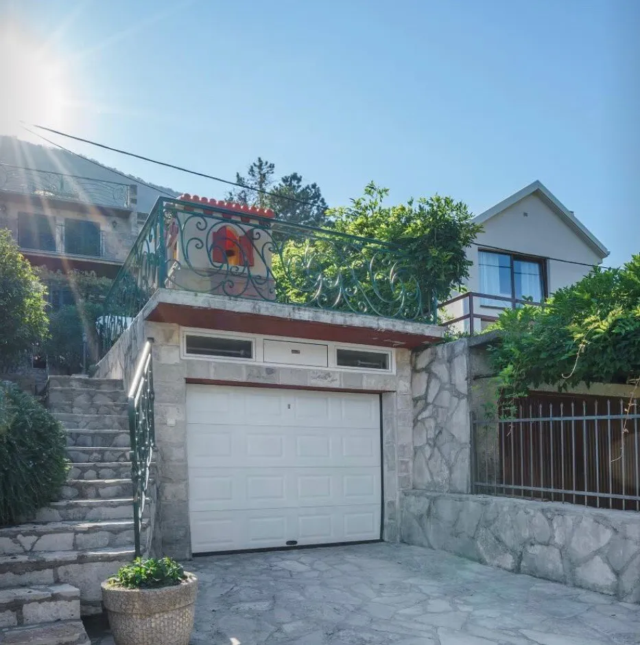 House exterior showing a white garage door, stone steps, and an ornate iron railing on the terrace.