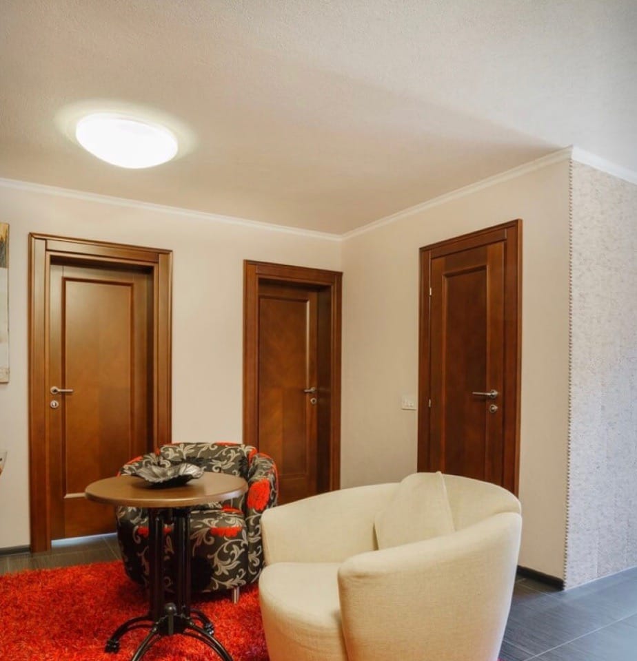 Living room interior in a villa in Stoliv, Montenegro: light walls, wooden doors, armchairs, and a red rug.