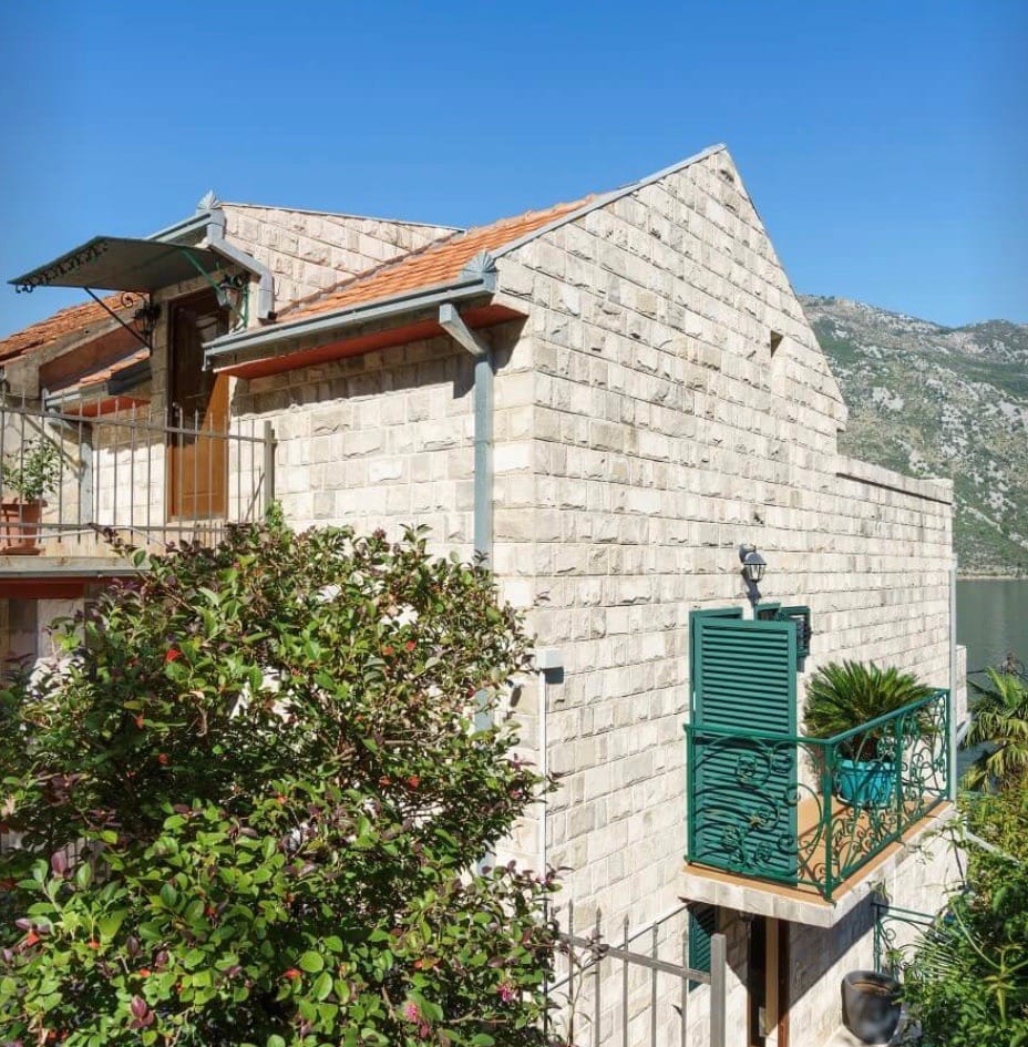 Stone villa in Stoliv, Montenegro: natural stone facade, green shutters, and a balcony with sea and mountain views.