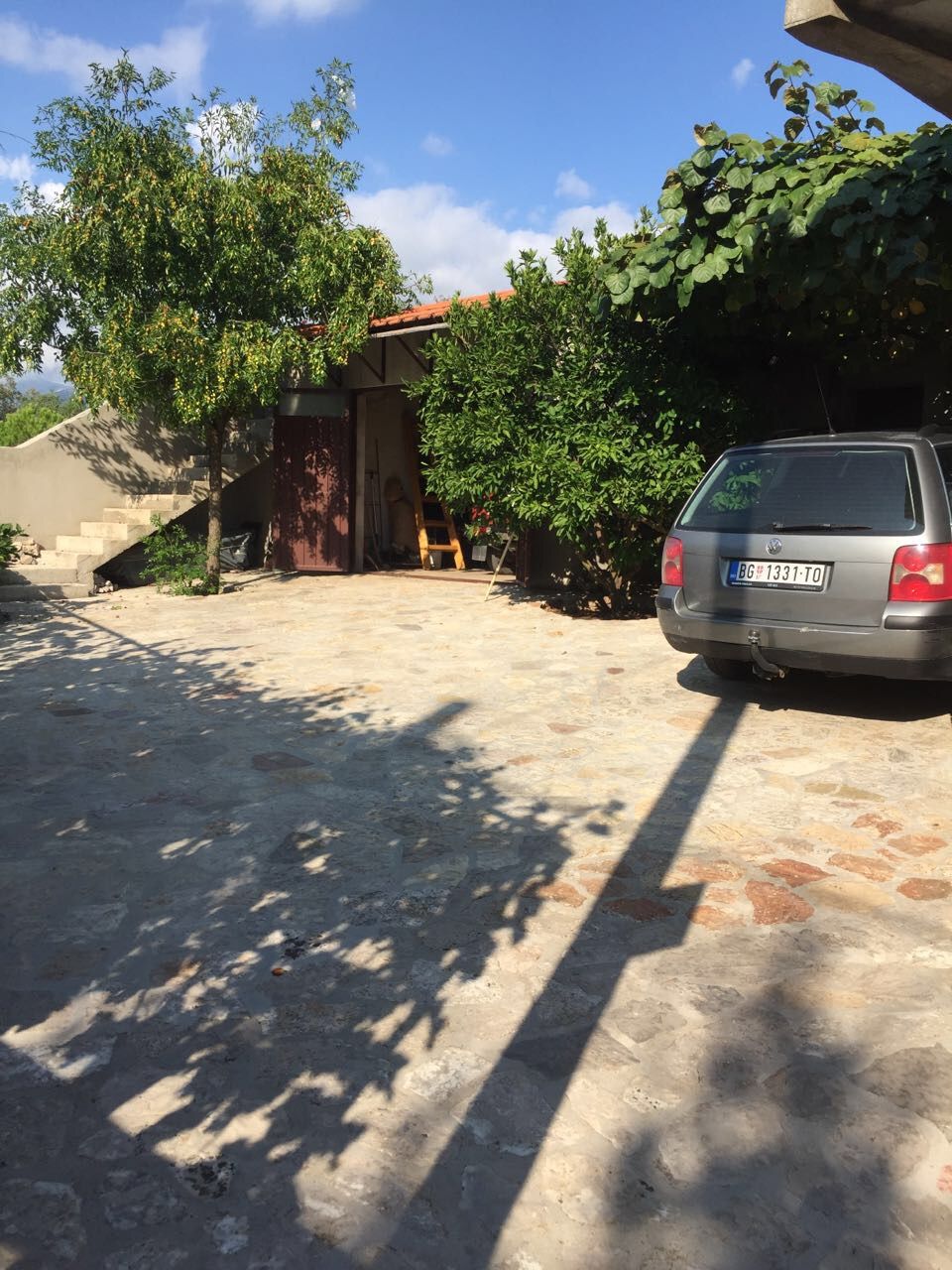 Courtyard of a house in Krimovica, Montenegro: stone patio, parking space, garage, and a green garden with trees.