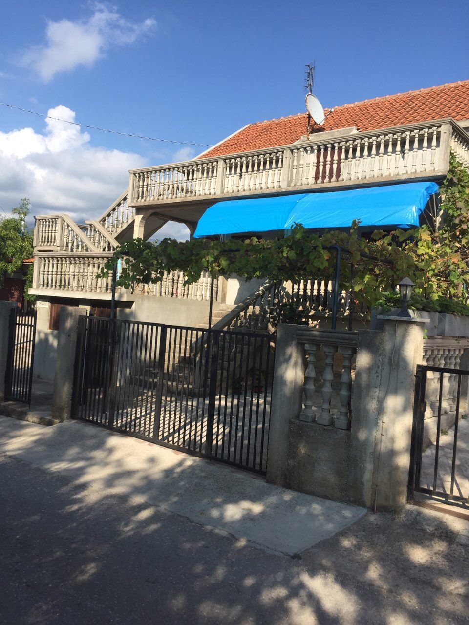 Two-story house in Krimovica, Montenegro: facade with a terrace, balustrade, vineyard, and metal gate.