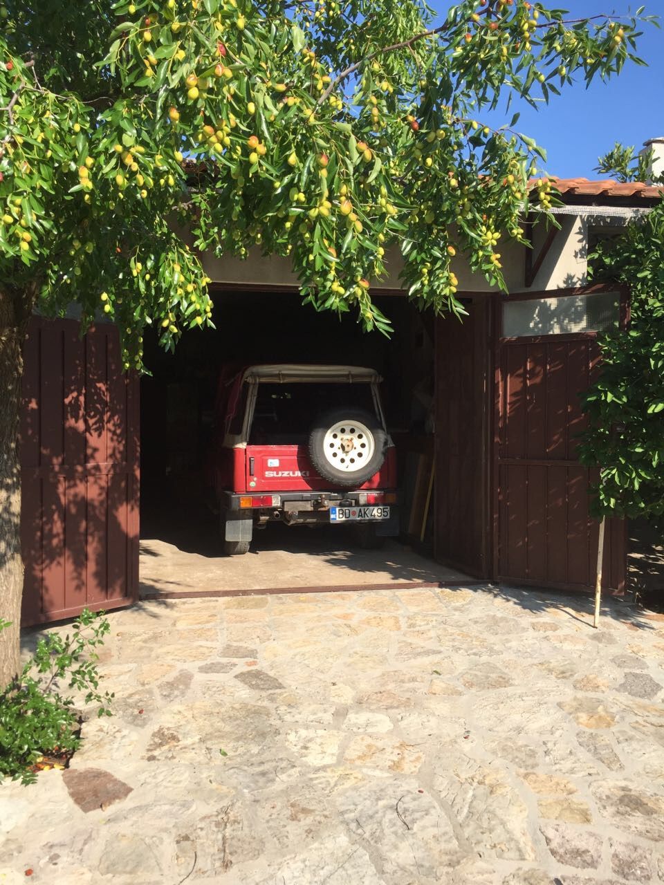 Garage with a car by a private house in Krimovica, Montenegro, with a stone patio and a fruit tree in the yard.