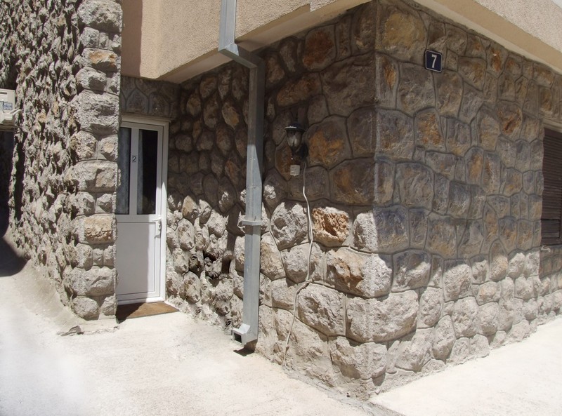 Entrance to the hotel in Bečići, Montenegro: building facade with natural stone finish and a white plastic door.