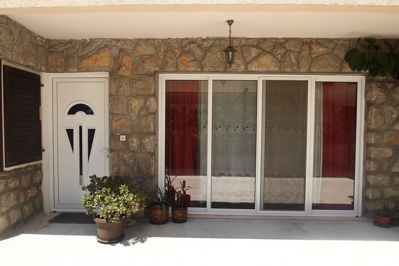 Entrance to hotel No. 844 in Bečići, Montenegro: natural stone facade, white plastic door, and panoramic windows.