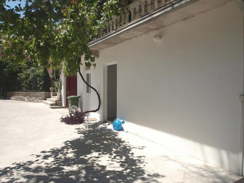White facade of a hotel in Bečići, Montenegro, with a terrace, grapevine, and entrance to a ground-floor room.