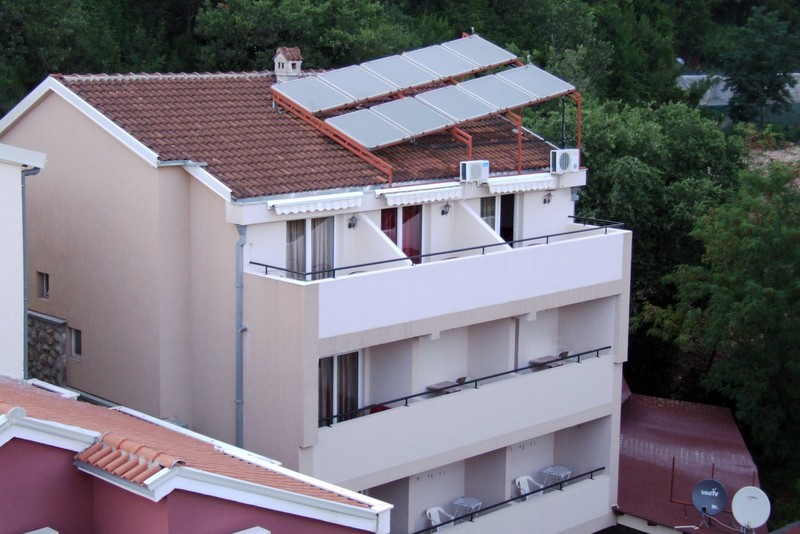 Facade of a hotel in Bečići, Montenegro: a building with balconies, a tiled roof, and installed solar panels.