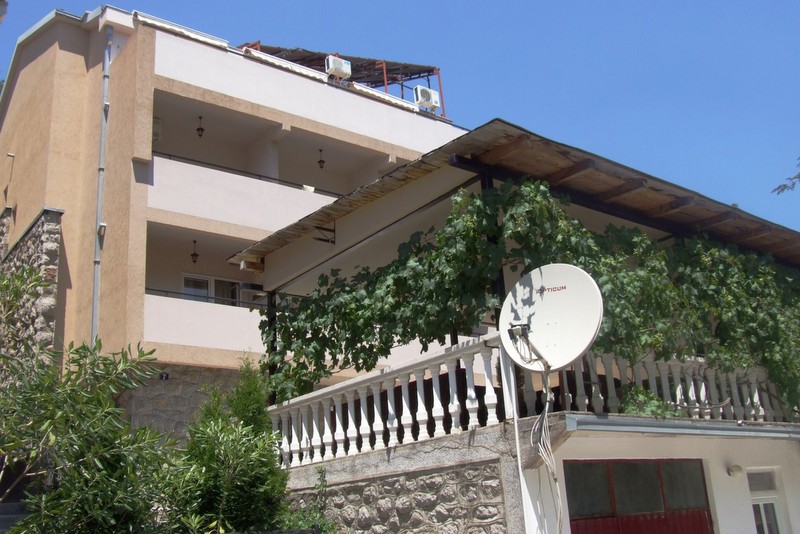 Three-story hotel in Bečići, Montenegro: facade with balconies, terrace with grapevine, and stone cladding of the base.