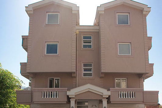 Facade of a three-story beige hotel with balconies and panoramic windows in Bečići, Montenegro.