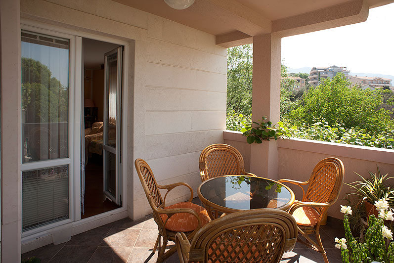 Cozy balcony with wicker furniture and a view of greenery at a hotel in Bečići, Montenegro. Terrace with a round table and chairs.
