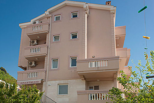 Facade of a four-story hotel in Becici, Montenegro, with balconies, air conditioners, and light stone cladding.
