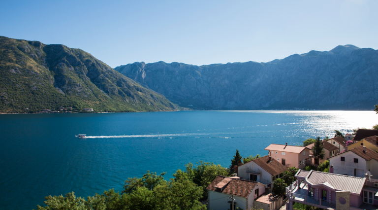 Panoramic view of the Bay of Kotor and mountains from a house in Stoliv, Montenegro: sea, a boat, and coastal buildings.