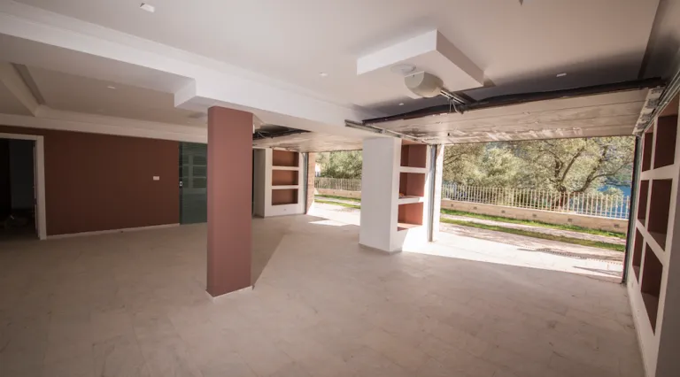 Large empty room with tiled floor, columns, built-in shelves, and an open view to a fenced yard.