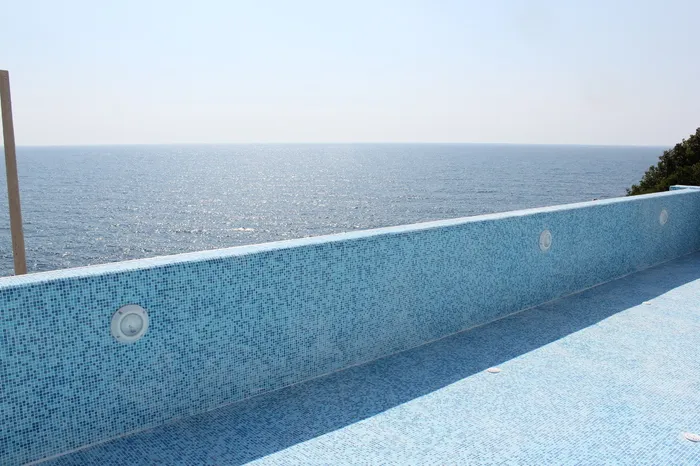 Pool with blue mosaic tiles and underwater lights overlooking the sea horizon.