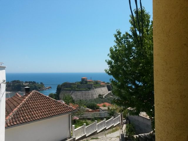 View from a balcony in Ulcinj, Montenegro: a panorama of the old fortress, the sea, and the city’s terracotta roofs.