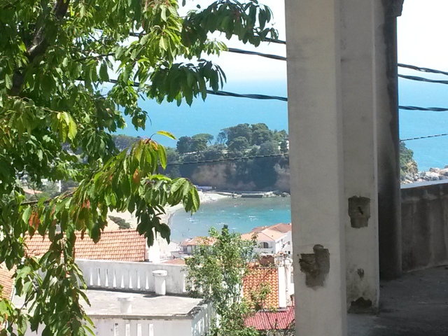 View from the balcony of a house in Ulcinj, Montenegro: a panorama of the sea bay, beach, and the city’s terracotta rooftops.