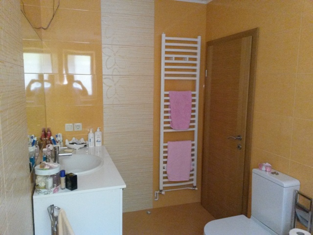 Bathroom in a house in Ulcinj, Montenegro: yellow tiles, white fixtures, towel warmer, and mirror.