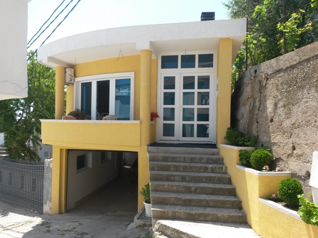 Yellow house in Ulcinj, Montenegro: facade with a terrace, panoramic windows, staircase, and an integrated garage on the ground floor.