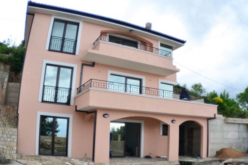 Three-story peach-colored house with balconies and a terrace in Shushan, Montenegro. Exterior view of the building facade.