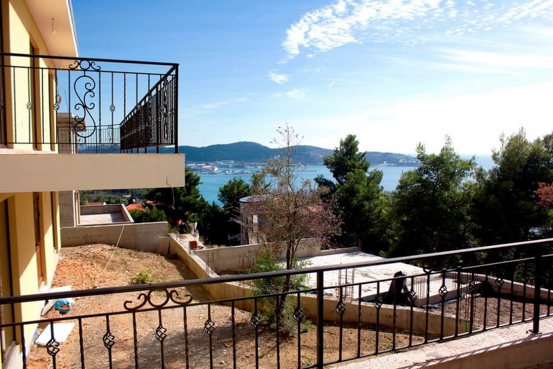 View from the balcony of a house in Shushan, Montenegro: wrought-iron railings, panoramic view of the sea, mountains, and a construction site.