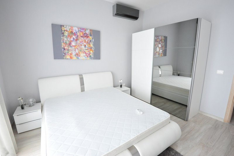 Modern bedroom with a white bed and mirrored wardrobe in an apartment in Dobri Vody, Montenegro.