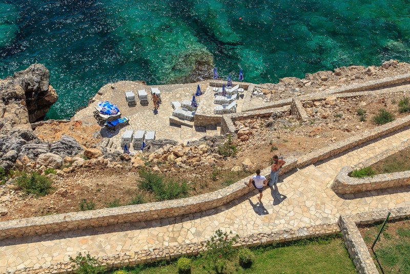 Top view of a private beach with sun loungers and the azure sea by a residential complex in Dobra Voda, Montenegro.