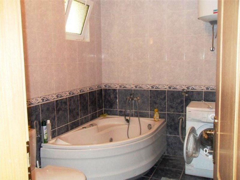 Bathroom with a corner bathtub and washing machine in a house, Shushan, Montenegro. Tiled finish, window in the bathroom.