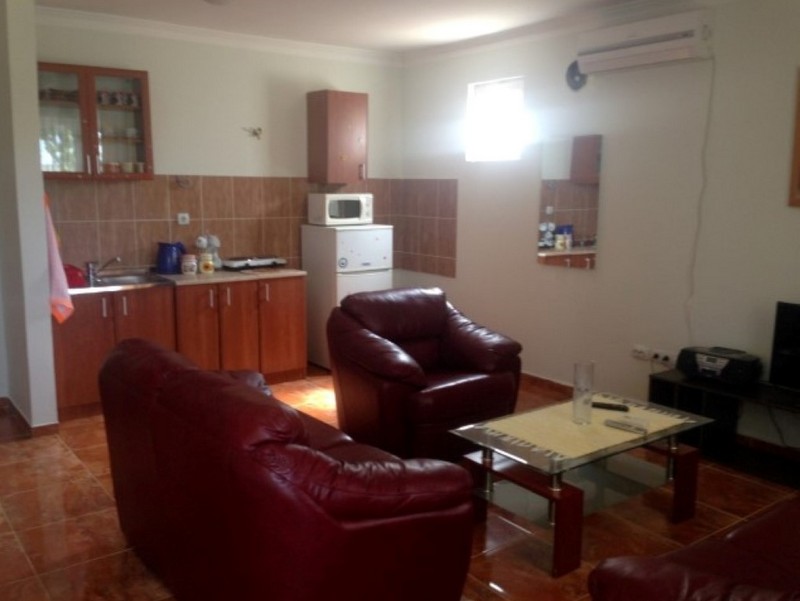 Living room with kitchen in a house in Shushan, Montenegro: red leather furniture, tiled floor, and kitchen cabinets.