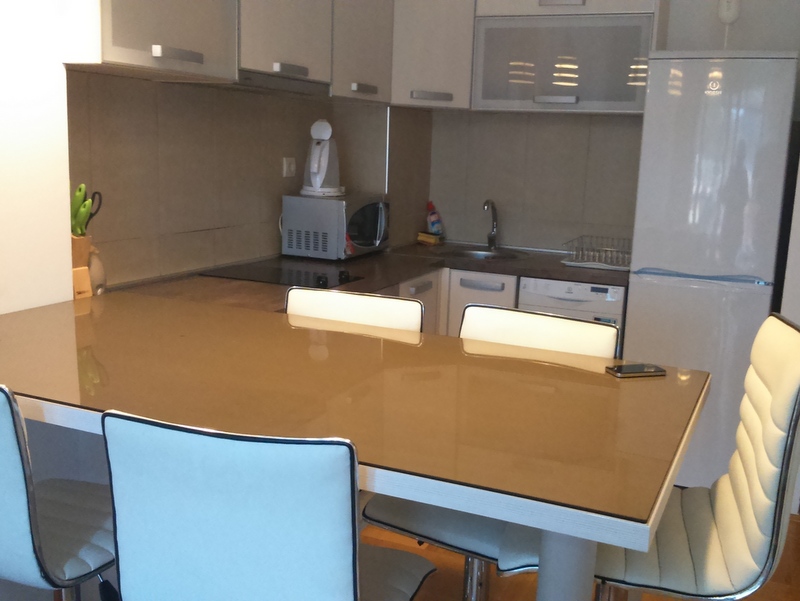 Modern kitchen with dining area in an apartment, Budva, Montenegro: light-colored cabinets, appliances, and a glass table.