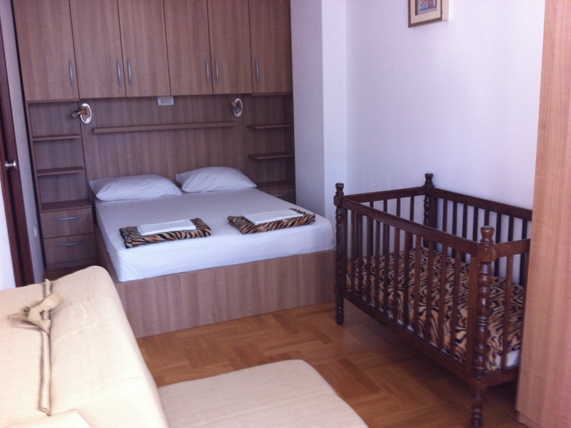Bedroom in an apartment in Budva, Montenegro: double bed with built-in wardrobe, crib, and parquet flooring.