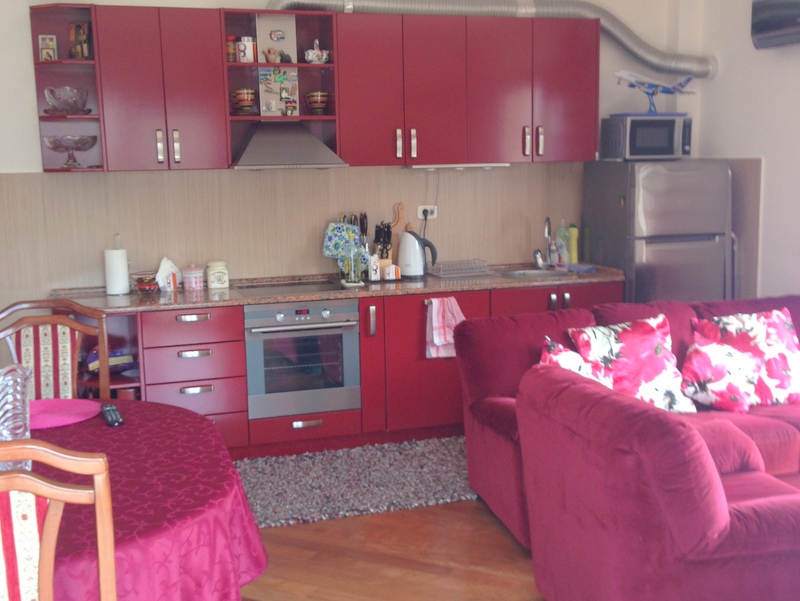 Kitchen-living room with a red kitchen set and a soft sofa in an apartment for sale, Budva, Montenegro.